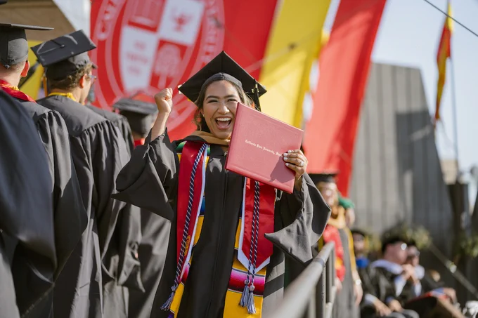 Smiling Stan State student holding their diploma. 