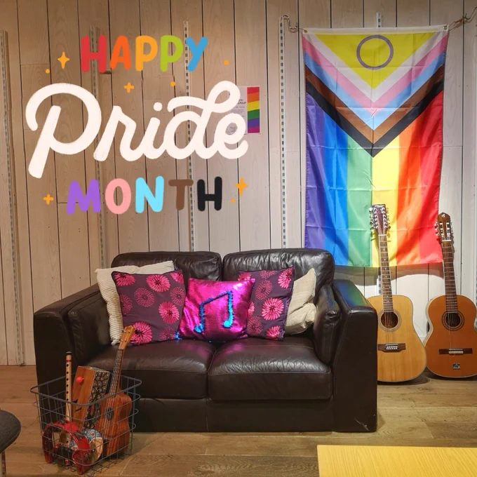 Pride flag hangs in the Hub above a sofa and guitars