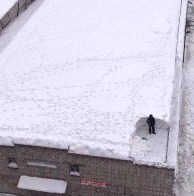 A man shoveling snow from a roof. He has only removed a very small portion.
