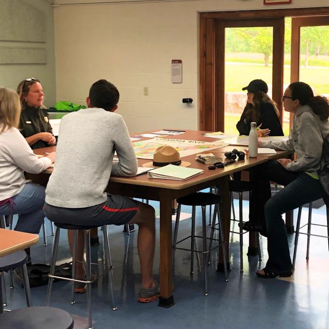A photo of five people sitting around a table having a discussion. 