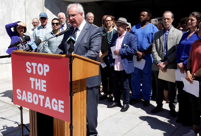Representative David Gomberg of the rural coast speaks about federal funding for rural communities at risk. The sign reads "STOP THE SABOTAGE"