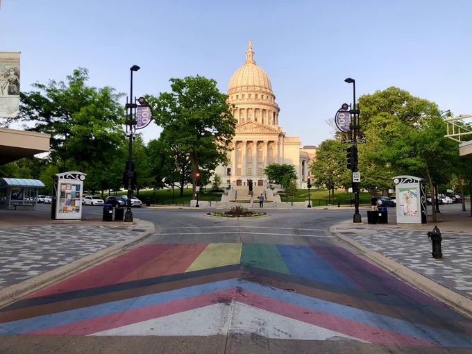 The capitol building in Madison, Wisconsin and a pride flag on the pavement nearby.
