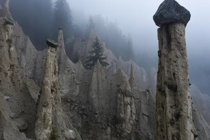A photograph of tall rock formations with trees in the background covered with fog. 
