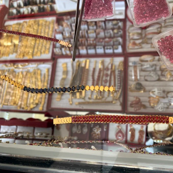 Photo of chains made of red, gold and black gemstones. Lots of other jewellery can be seen in the displays behind these chains