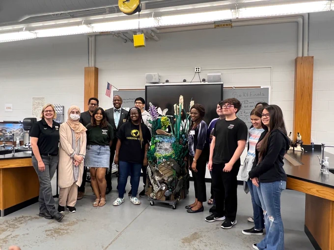 A group of high school students and teachers standing around a large, colorful sculpture.