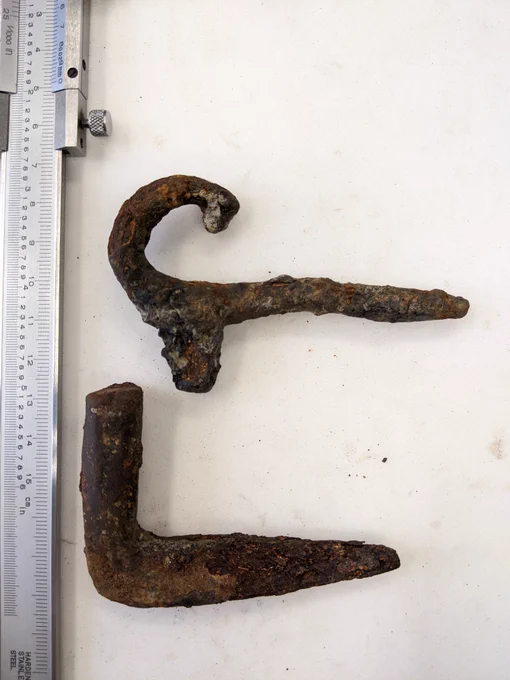 Two rusty iron objects. Top is a curled hook shape. Bottom is an L-shaped pivot.