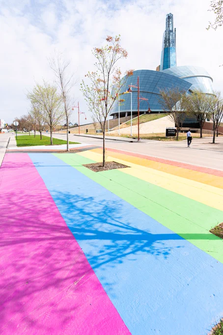An external shot of the Museum during the day. The foreground shows a crosswalk painted with rainbow stripes and triangles, creating the Progressive Pride flag.