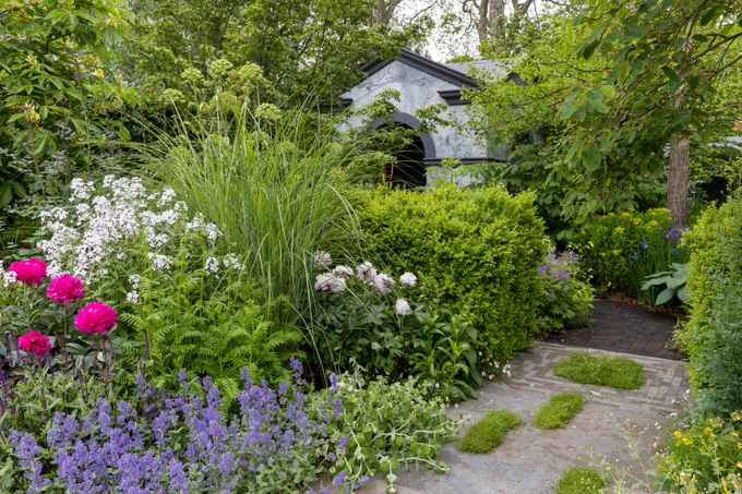 Blue, pink, white and green planting with a hut in the background.