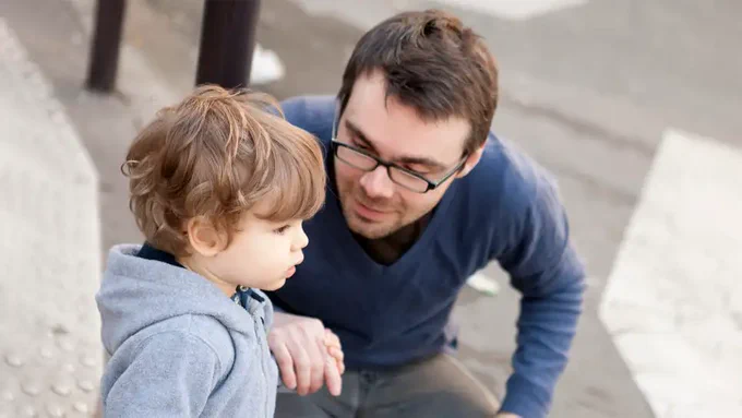 Adult man crouching next to a toddler and talking to him.