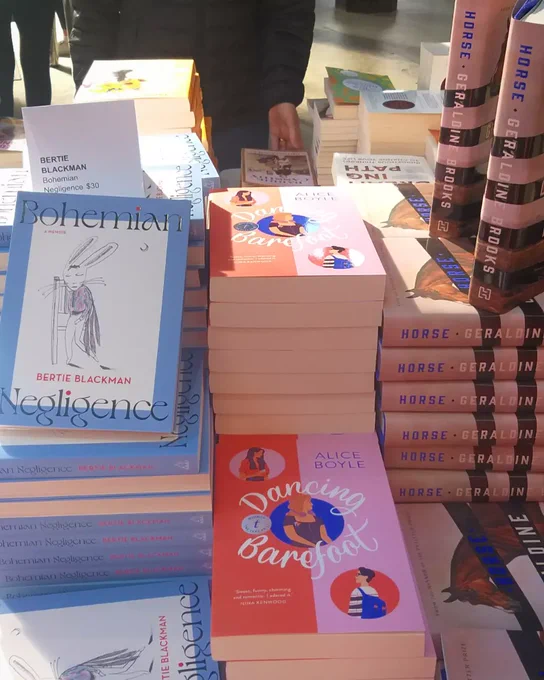 Stacks of books sitting on a sunny table, including 'Dancing Barefoot' by Alice Boyle.