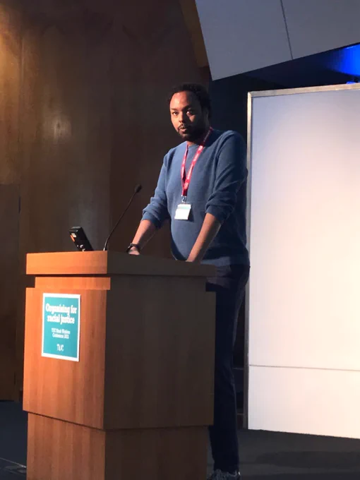 Up on stage in front of a lectern speaking.