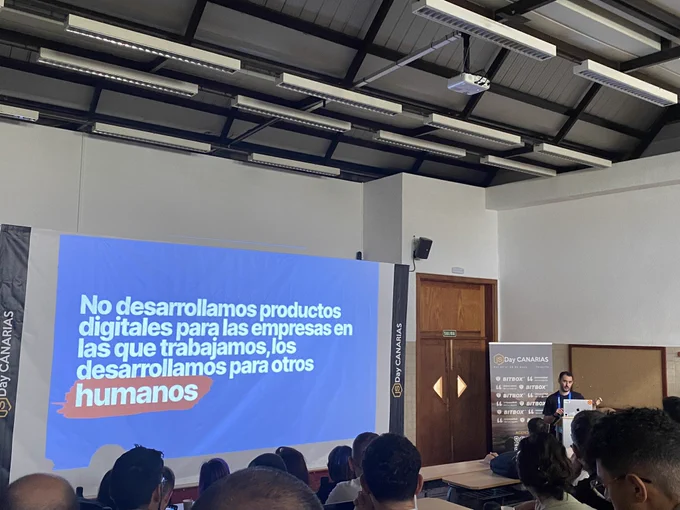 Adrian bolonio giving a talk at the JS Day Canarias conference. A screen showing the sentance in spanish : “No desarrollamos productos digitales para las empresas en las que trabajamos, los desarrollamos para otros humanos”
