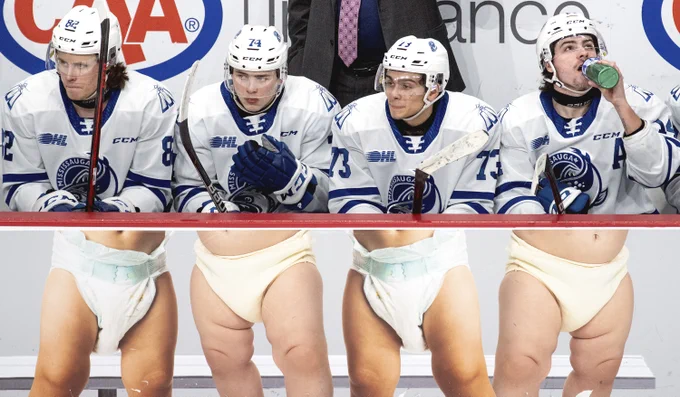 An advertisement on the side of the visitors’ bench makes, from left, Callum Chisholm (82), Zander Veccia (74), Luca Del Bel Belluz (73) and James Hardie (14) of the Mississauga Steelheads appear as infants during a regular season Ontario Hockey League game at the Meridian Centre, in St. Catharines, Ont., on Feb. 1, 2022. (Alex Lupul/Freelance)