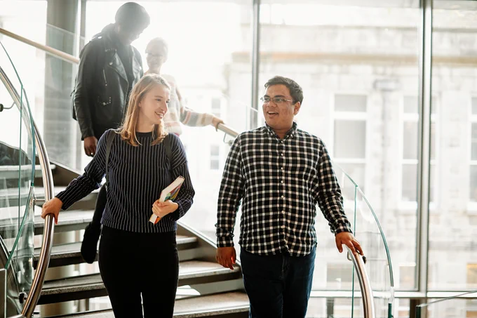 Four international Tangent school students descend the spiral staircase in the Trinity College Dublin business school, chatting about coursework. 