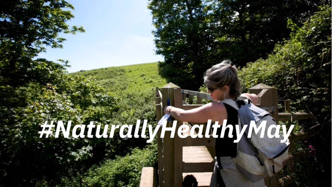A woman climbing a stile. Text reads: “Naturally Healthy May”
