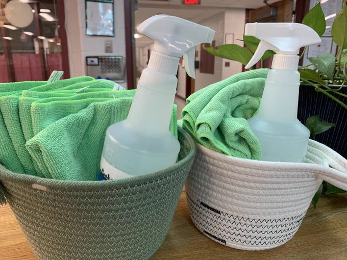 Baskets with a bottle of cleaning spray and green cleaning cloths.