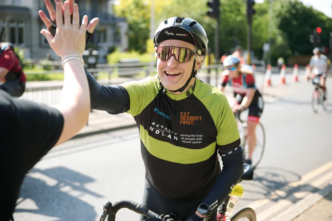 an Anthony Nolan cyclist giving a high five to a supporter whilst looking towards the camera
