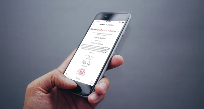 A hand holding a cell phone showing a digital diploma.