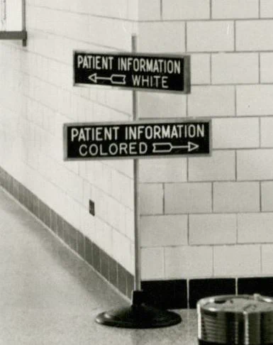 Detail from a 1953 photo showing a sign displaying directions for "Patient Information White" and "Patient Information Colored."