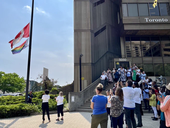 Attendees are standing outside and watching the flags being raised. 
