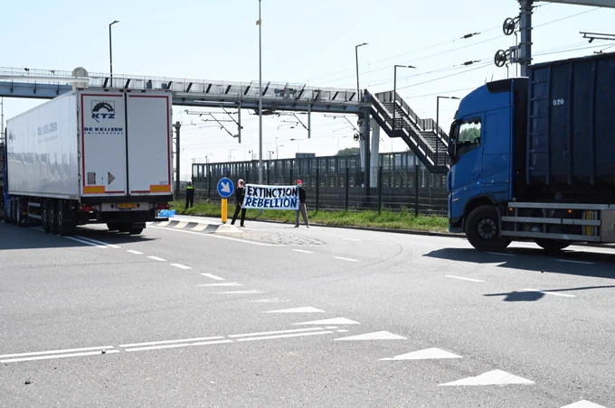 Twee actievoerders blokkeren de weg met een spandoek waarop Extinction Rebellion staat.