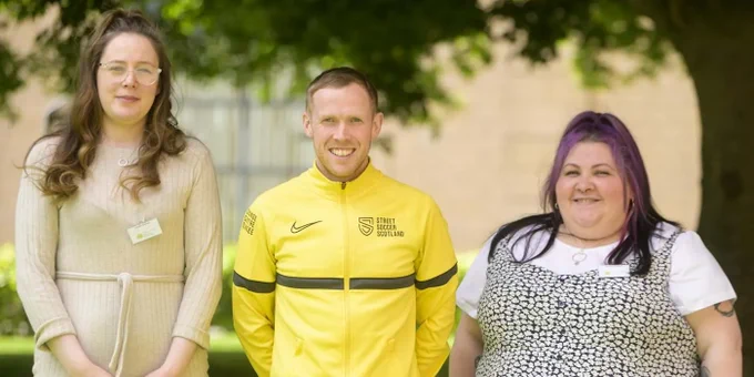 Sarah, Kyle and Paula stand outdoors. They smile directly to camera.