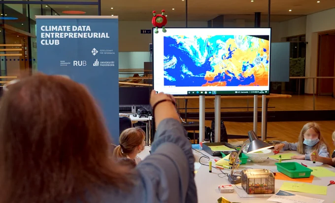 Jugendliche bei einem interaktiven Workshop. Auf dem Bildschirm in der Mitte des Raumes sind Satellitendaten angezeigt. 