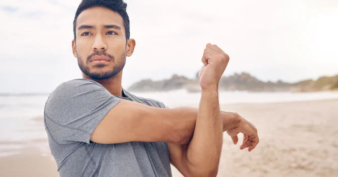 Asian man stretching on a beach.