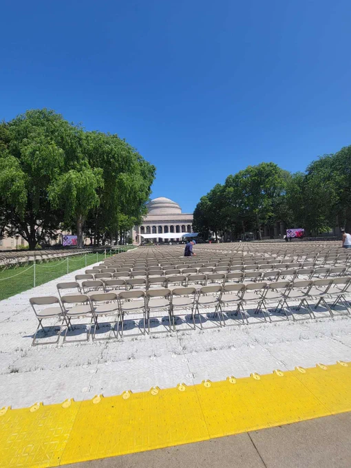 Killian Court is prepared for a commencement ceremony with hundreds of chairs lined in rows. The sky is clear and blue.