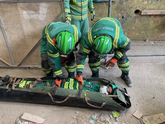 A picture of a training session where Hazardous Area Response Team medics are practising the rescue of a patient from a collapsed building. Three medics are about to carry a colleague in a special stretcher. 