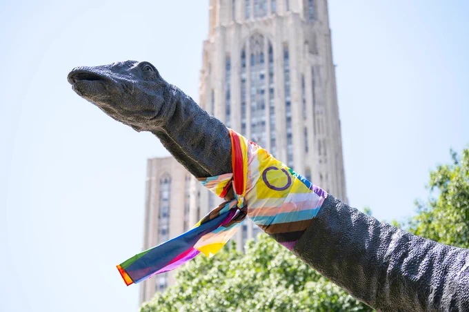 Dippy the Dinosaur wears a Pride flag as a scarf in front of the Cathedral of Learning