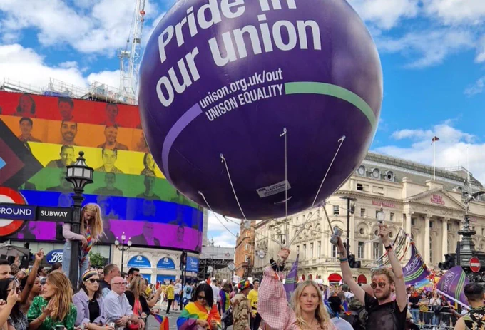 Pride event at Piccadilly Circus, London. UNISON big purple balloon overhead reads Pride in our union unison.org.uk/out Unison equality