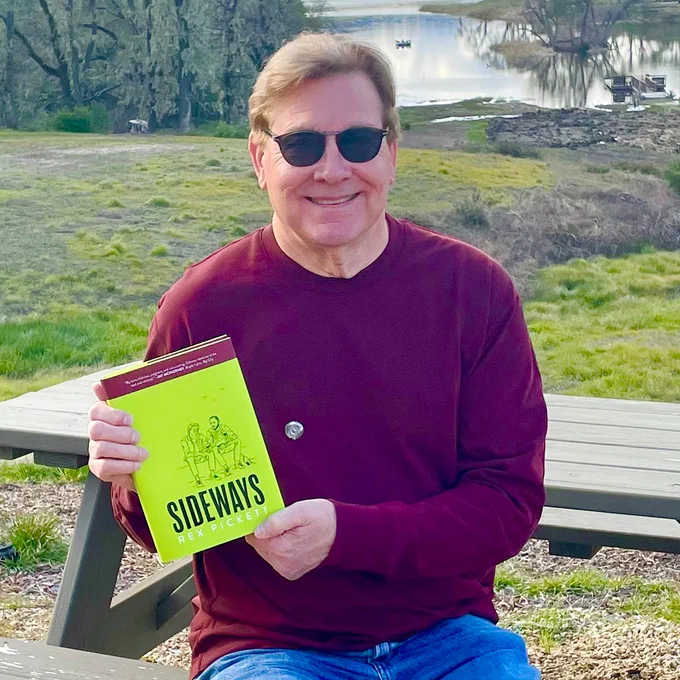 Rex Pickett, author of "Sideways" sitting outside on a picnic table holding his new book "Sideways Chile." 