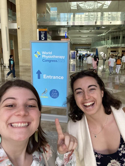 Photo of myself and my friend Noemie smiling very happily and pointing to an entrance sign saying “world physiotherapy congress 2023”