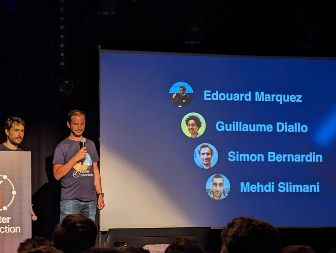 Photo de la scene de la conférence, une slide montre les noms d'une partie des membres de l'organisation : Edouard Marquez, Guillaume Diallo, Simon Bernardin et Mehdi SLIMANI