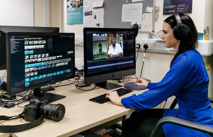 Sophie sitting in front of two camera monitors editing interview footage from the expedition. 