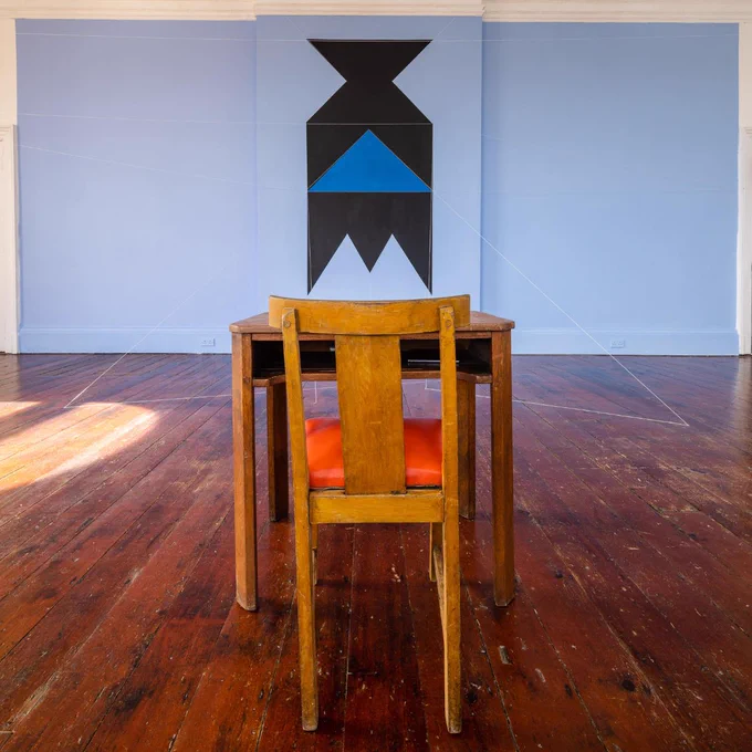 Image: View of Patrick Ireland, aka Brian O'Doherty, HCE Redux, 2004 (remade 2023), SIRIUS, 2023. Paint, cord, table, chair, typed paper. Dimensions variable. Courtesy of The Estate of Brian O’Doherty. Photograph: John Beasley – in a large room: in the foreground a the back of a chair at a small table, both wooden; on the wall some 5 metres (?) further into the room, a geometrical pattern on the pale-blue wall; some strings link the pattern to the floor • "The SIRIUS Summer School examines the relationship between art and politics. The 2023 edition explores the practice of the Irish artist Brian O’Doherty (1928–2022) and the location of SIRIUS. One, Here, Now is the title O’Doherty gave the mural he carried out at SIRIUS in 1996; Cobh is from where he emigrated to the United States in 1957. All of this leads us to consider the art ecosystem’s various affordances and potentialities, and what a visionary, strategic artist such as O’Doherty can offer toward our interventions (through…"