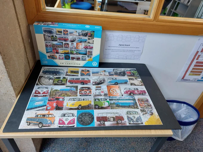 a completed jigsaw puzzle with its box standing up behind it. The jigsaw image is a grid of vintage VW campervans