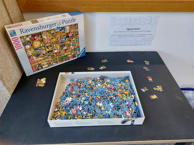 a box full of jigsaw puzzle pieces on a black board, surrounded with some individual pieces and the box lid standing up behind the box