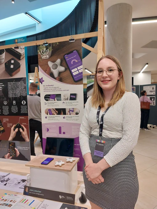 Image of student Jule Loescher standing in front of her project stand with a poster and products displayed in background. 