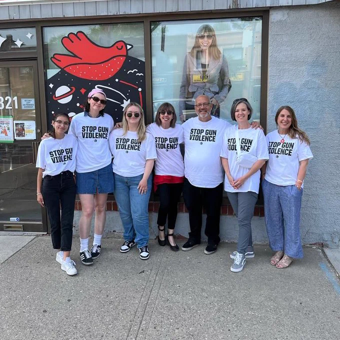 7 people standing together and smiling wearing white T-shirt’s saying “Stop Gun Violence”