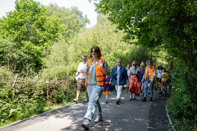 A woman in a hi-vis jacket leads a group along a forest path