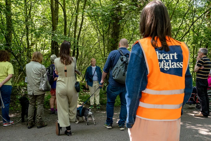 A woman speaks before a crowd of people, underneath green trees