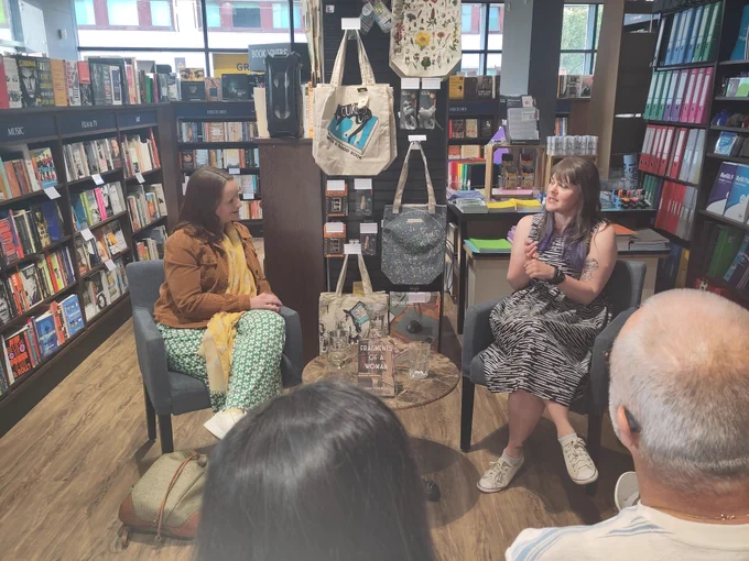 The author in conversation with interviewer, book placed between them. 