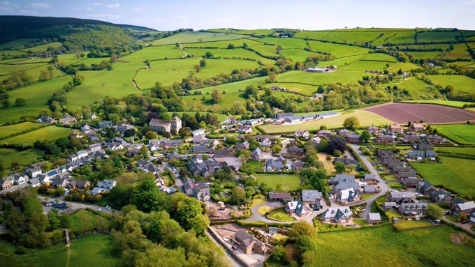 Photo of a town in the sprawling green UK countryside against a blue sky.
