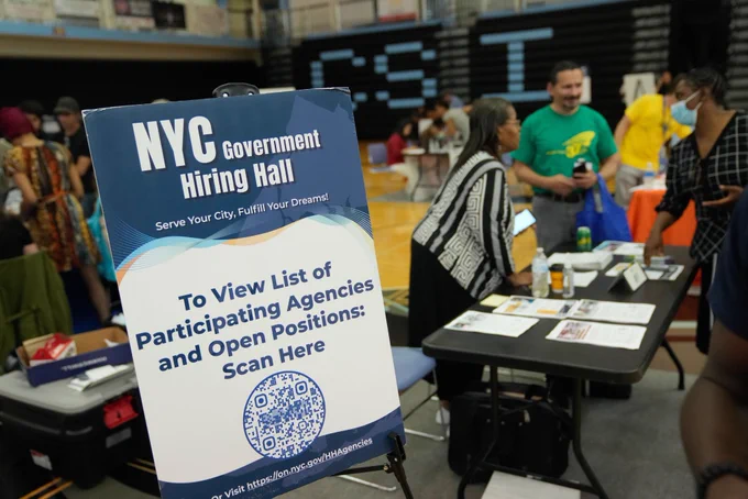 A sign reading "NYC Government Hiring Hall" in a busy gymnasium.