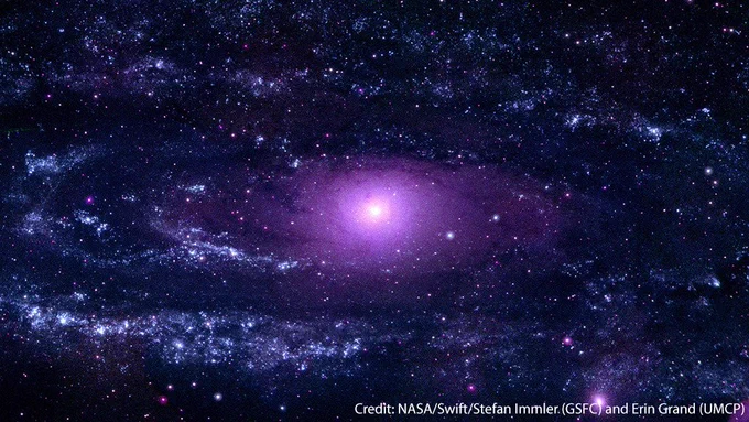 This is an image of the Andromeda galaxy captured by Swift in ultraviolet (UV) light. At the middle of the galaxy is a lavender colored circle that shines brightly at the galactic center, surrounded by a round cloud of darker purple. Around it are dark faint spiral arms that start at the center and spread outward, filling the rest of the image. Each of the arms are filled with large cloud-like clusters of bright blue-white dots. Glittered throughout are about 20,000 UV sources in various tones of purple dots that represent the countless stars in the Andromeda Galaxy. The brighter white clumped spots in the image show where star clusters lie. This image is watermarked with “Credit: NASA/Swift/Stefan Immler (GSFC) and Erin Grand (UMCP).”