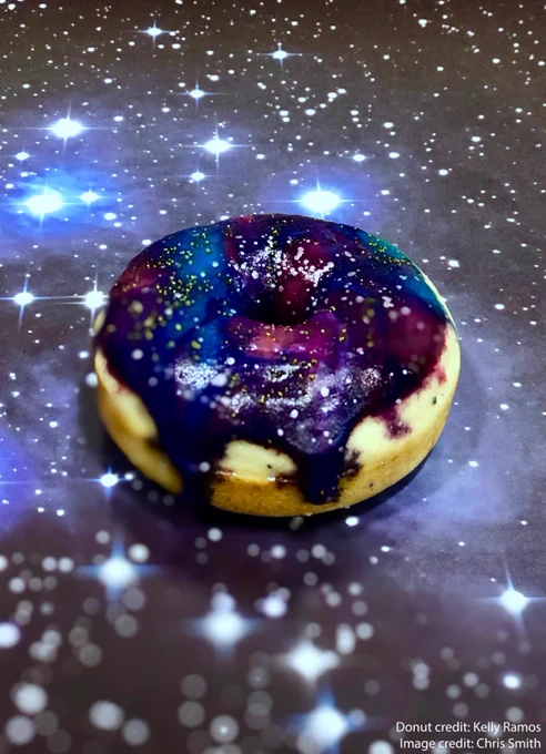This is a photo of a homemade donut with galaxy themed frosting and gold and silver edible glitter. The frosting is a swirling combination of purple, blue, and pink. The frosting is slightly dripping down the side of the light yellow cake donut, which is sitting on top of a poster of a starry background covered with various sizes of stars and light blue clouds of gas and dust. This image is watermarked with “Donut credit: Kelly Ramos” and “Image credit: Chris Smith.”