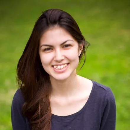 Victoria Sayo Turner smiles in a grey shirt in front of nature