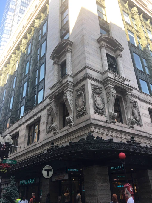 A build clad in stone houses a Primark store on the ground level, as well as a public fire alarm and an MBTA roundel at the building’s corner.